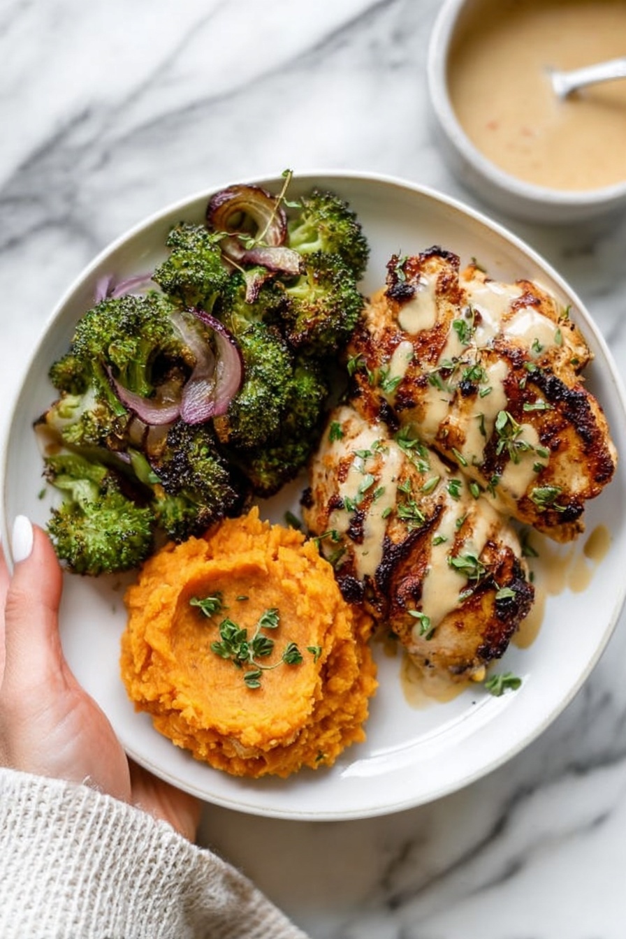 A white plate holds three main layers: the top layer is a piece of grilled chicken with dark grill marks and light creamy sauce drizzled on top, garnished with green herbs; to the left side, there is a generous serving of cooked broccoli and slices of cooked red onion with a slightly charred texture; below the chicken and broccoli, there is a portion of smooth, orange mashed sweet potatoes with some light sauce drizzled over it and tiny herb pieces sprinkled on top. The plate is placed on a light gray cloth on a white marbled surface, with gold fork and knife on the right side, and a bowl of creamy sauce is partially visible in the upper right corner, photo taken with an iphone --ar 2:3 --v 7